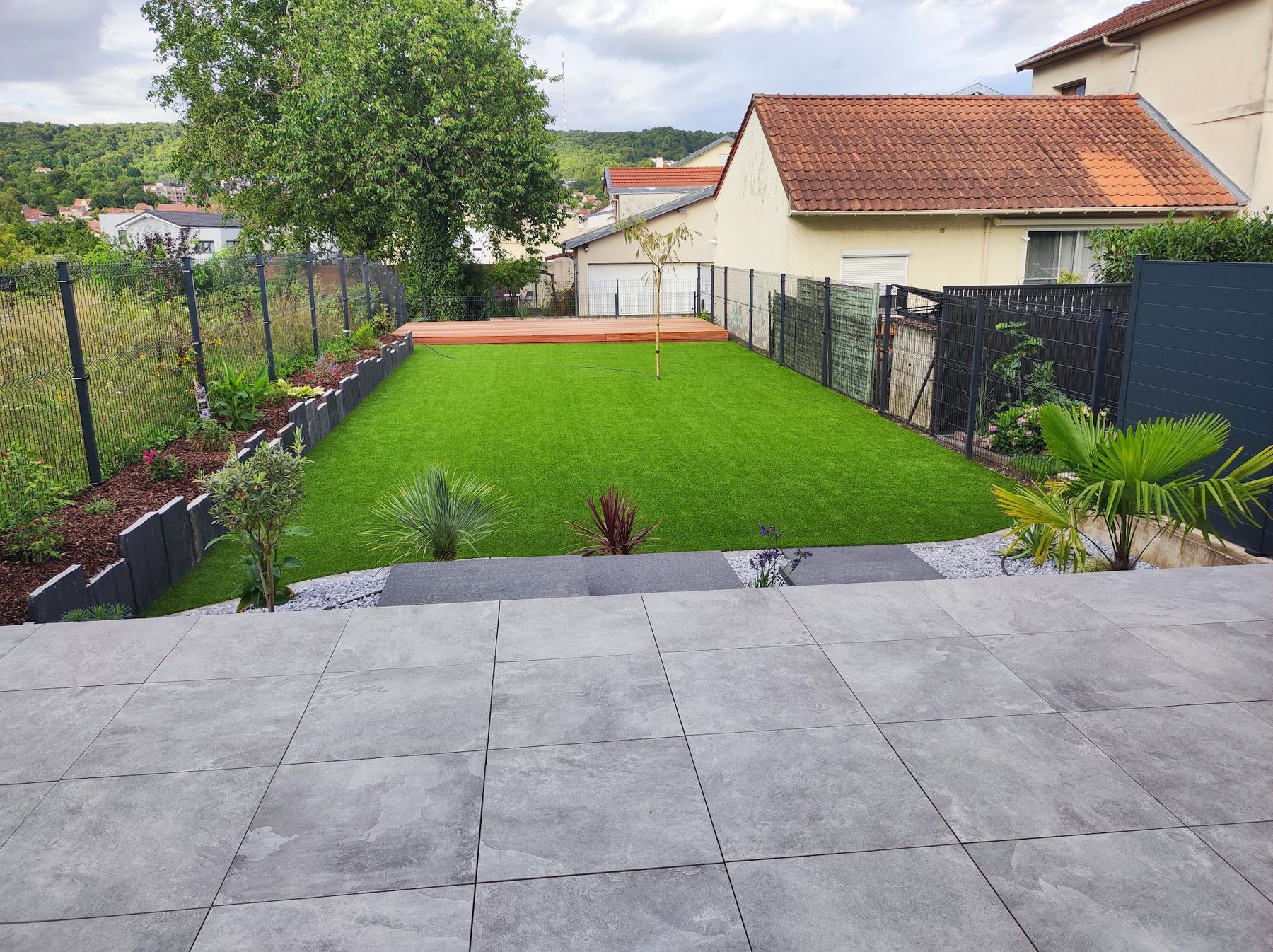Terrasse en grandes dalles grises, gazon et massifs bordés d'ardoise